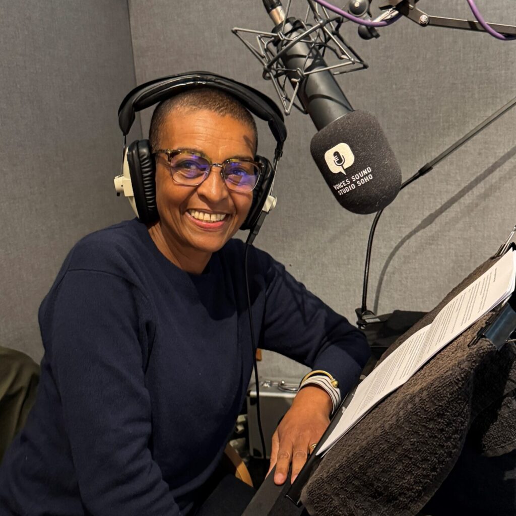 Photo of the actor Adjoa Andoh sitting in front of a microphone in a recording studio