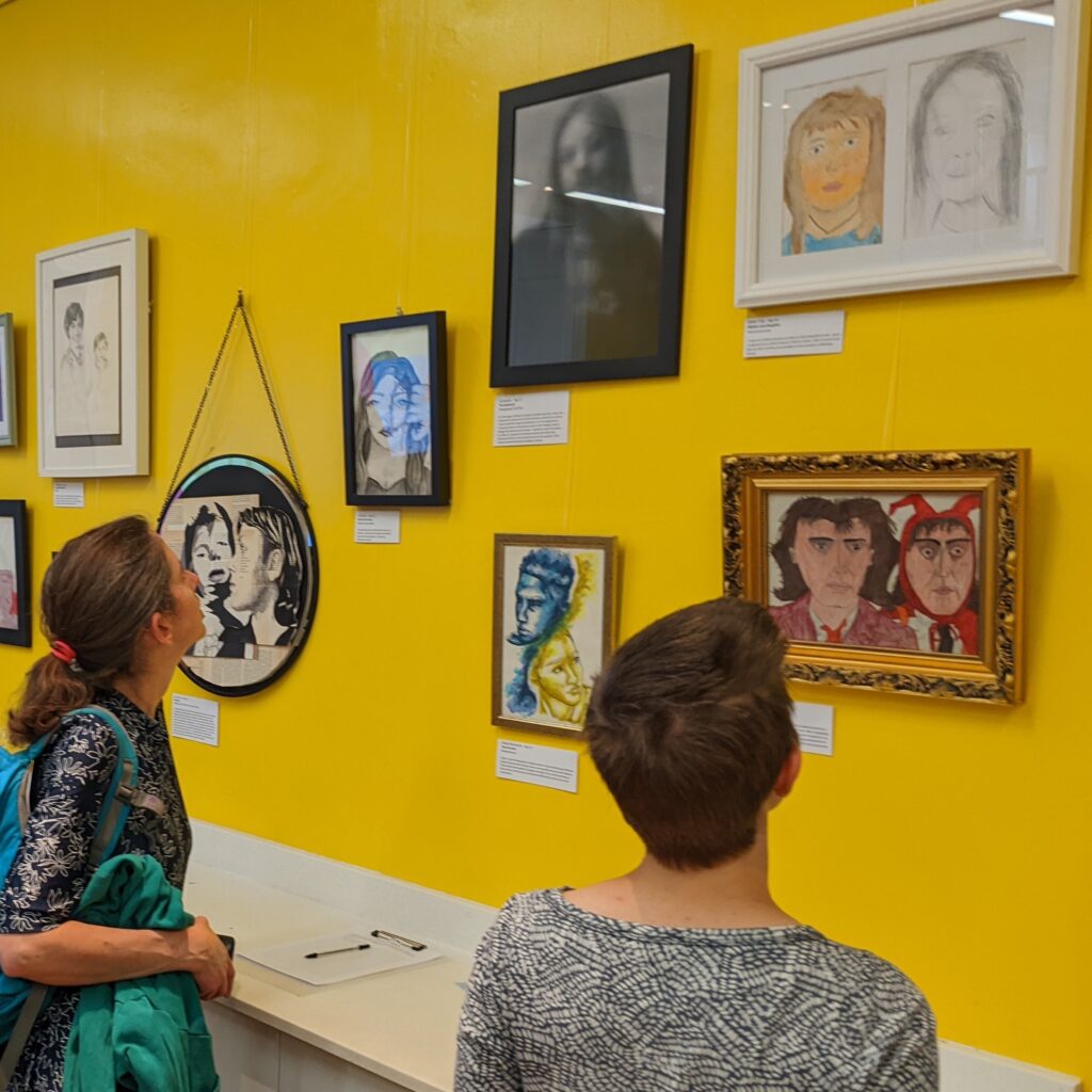 Photo showing people looking at artworks hung on a bright yellow wall