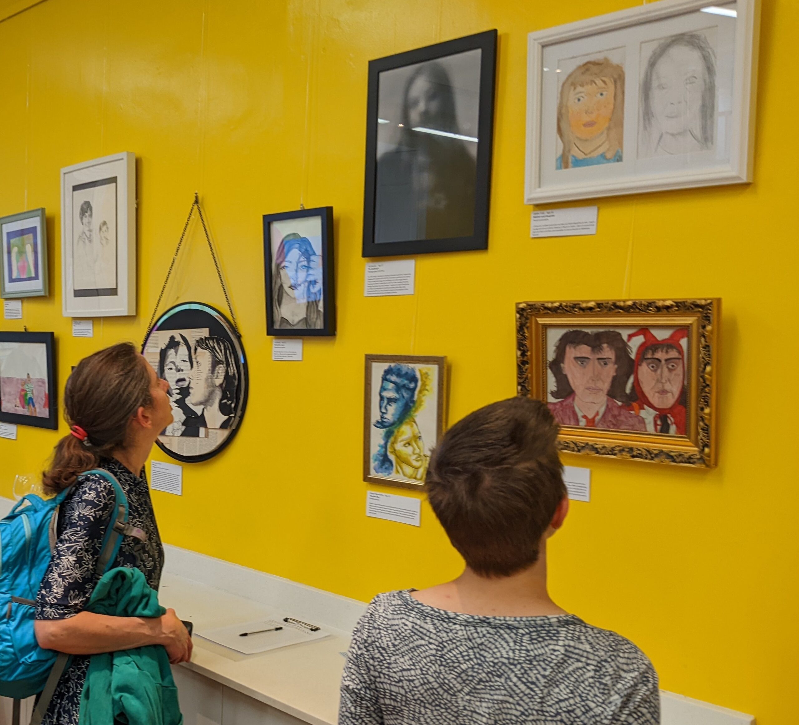 Photo showing people looking at artworks hung on a bright yellow wall
