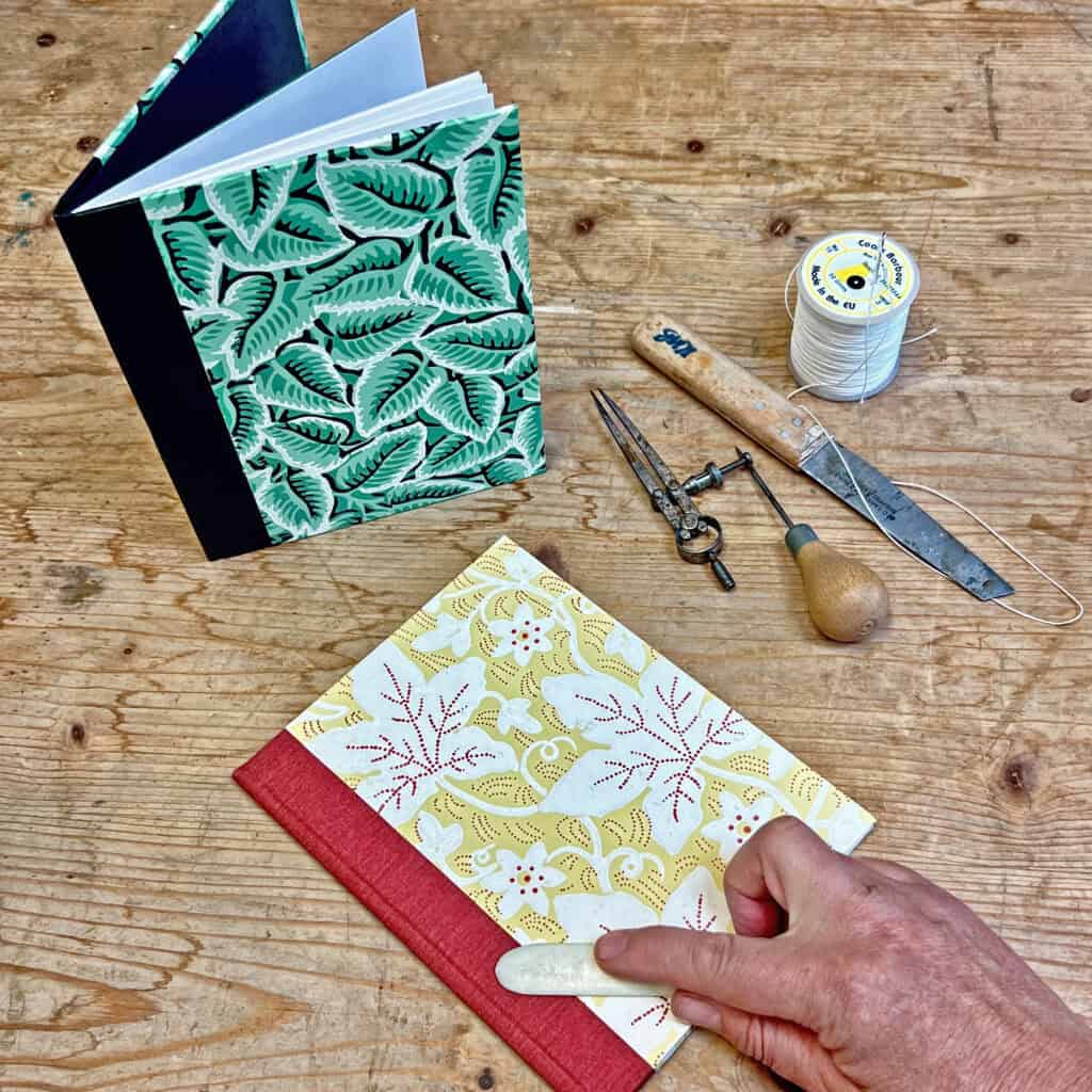 Two books on a table with some tools and a hand