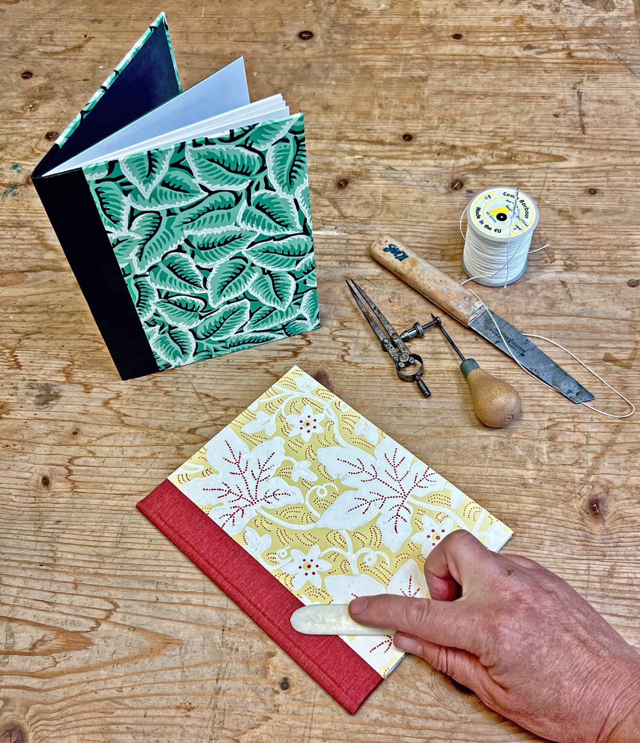 Two books on a table with some tools and a hand