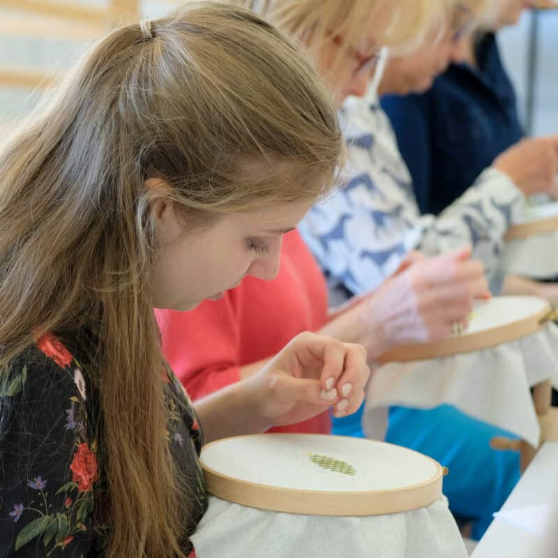 Young girl and ladies bending over needlework frames