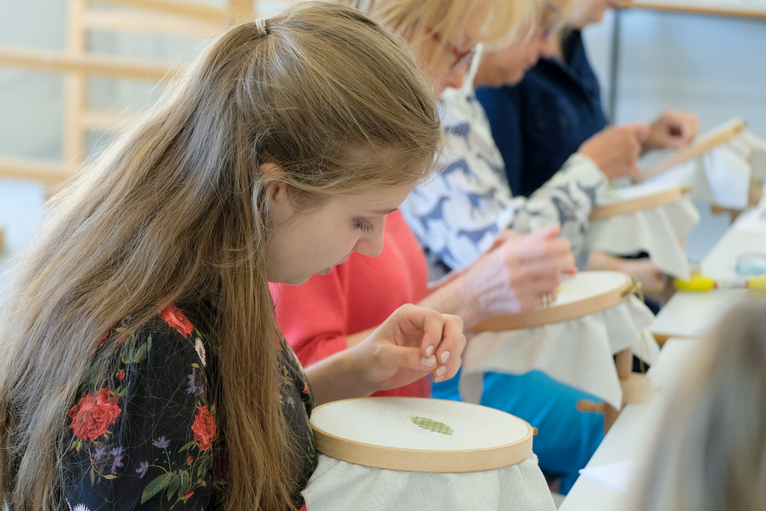 Young girl and ladies bending over needlework frames
