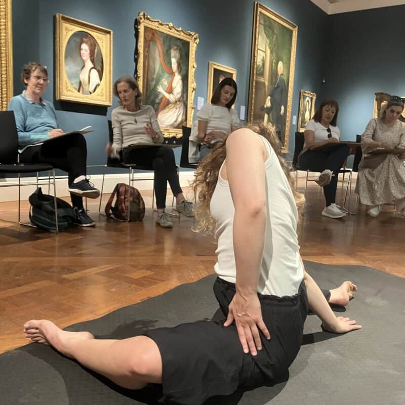 Woman in foreground in a splits position with seated people drawing her behind her