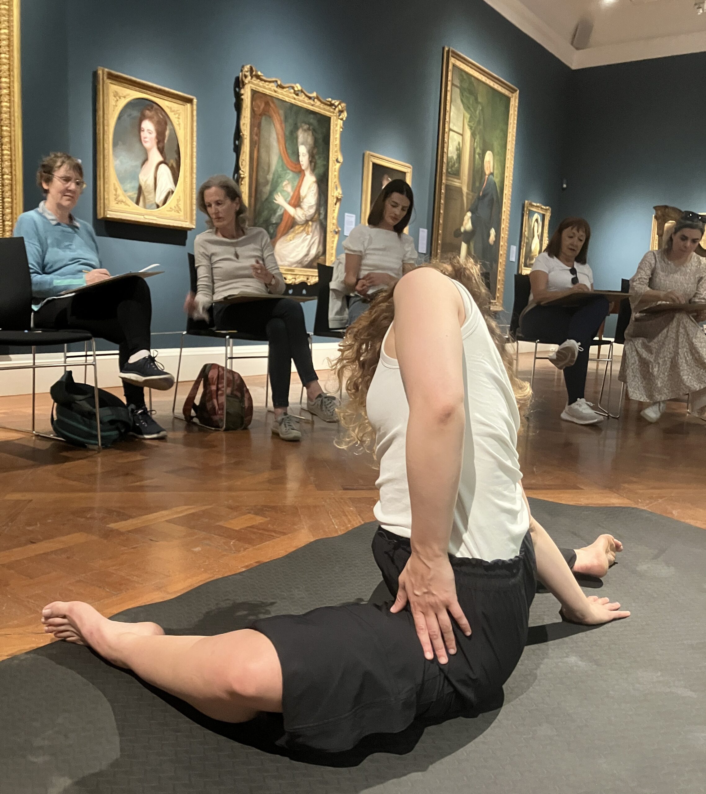 Woman in foreground in a splits position with seated people drawing her behind her