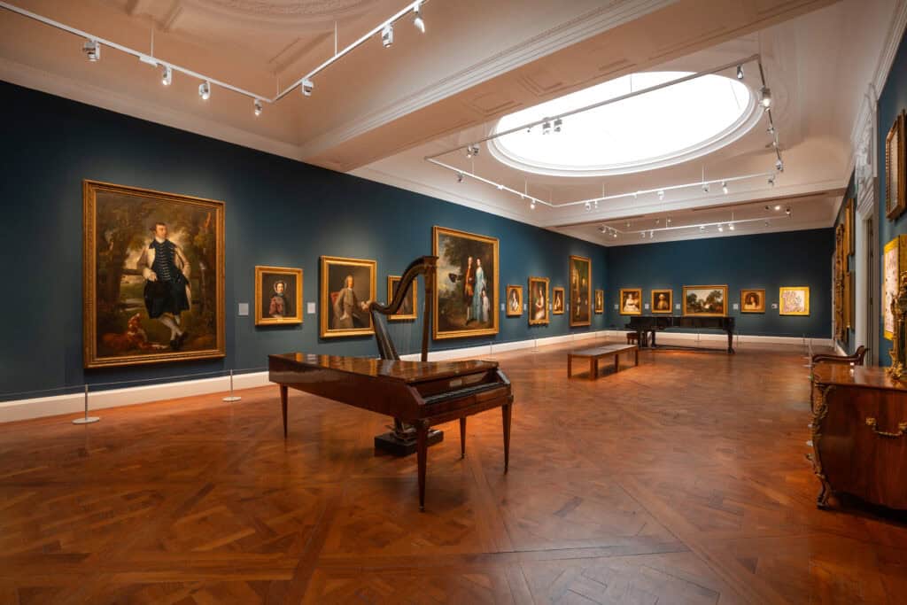 Photo of a large gallery with dark blue walls, portrait paintings in gold frames and historic musical instruments