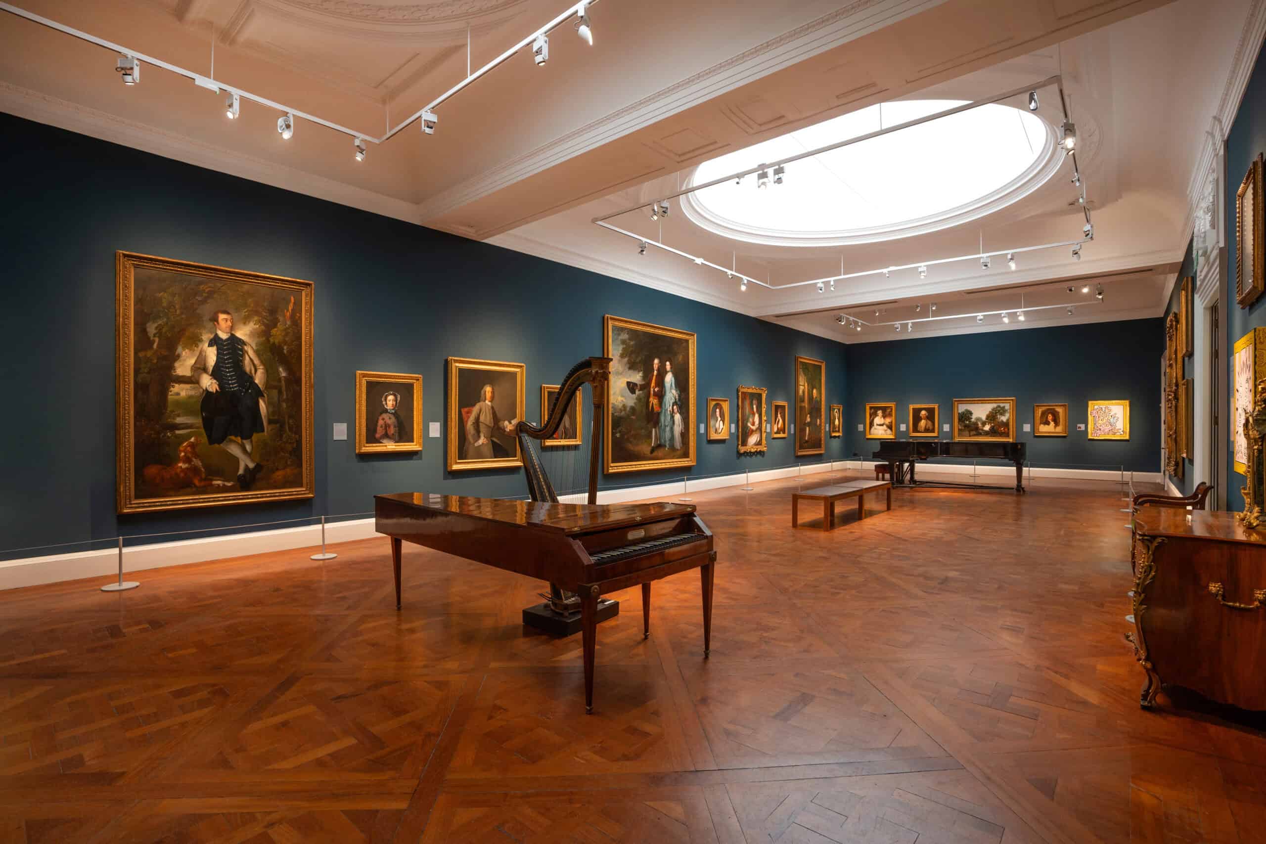 Photo of a large gallery with dark blue walls, portrait paintings in gold frames and historic musical instruments