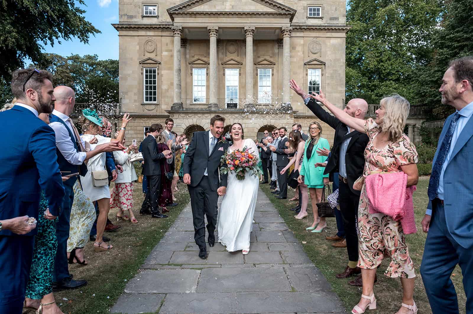 Photo showing a newly married couple walking down the path of the museum while their friends and family shower them in confetti