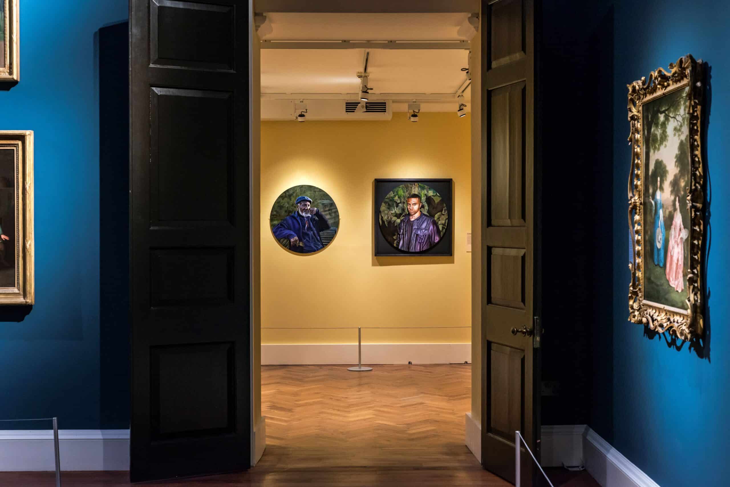 Looking through a dark doors to the yellow walls of the Donkor exhibition, showing 2 works