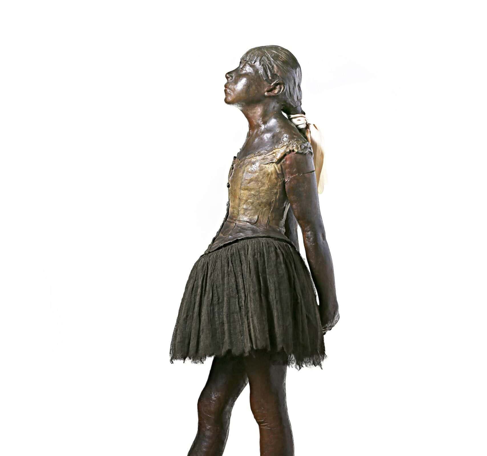 A bronze sculpture of a little girl in a ballet tutu with her arms behind her back, looking up