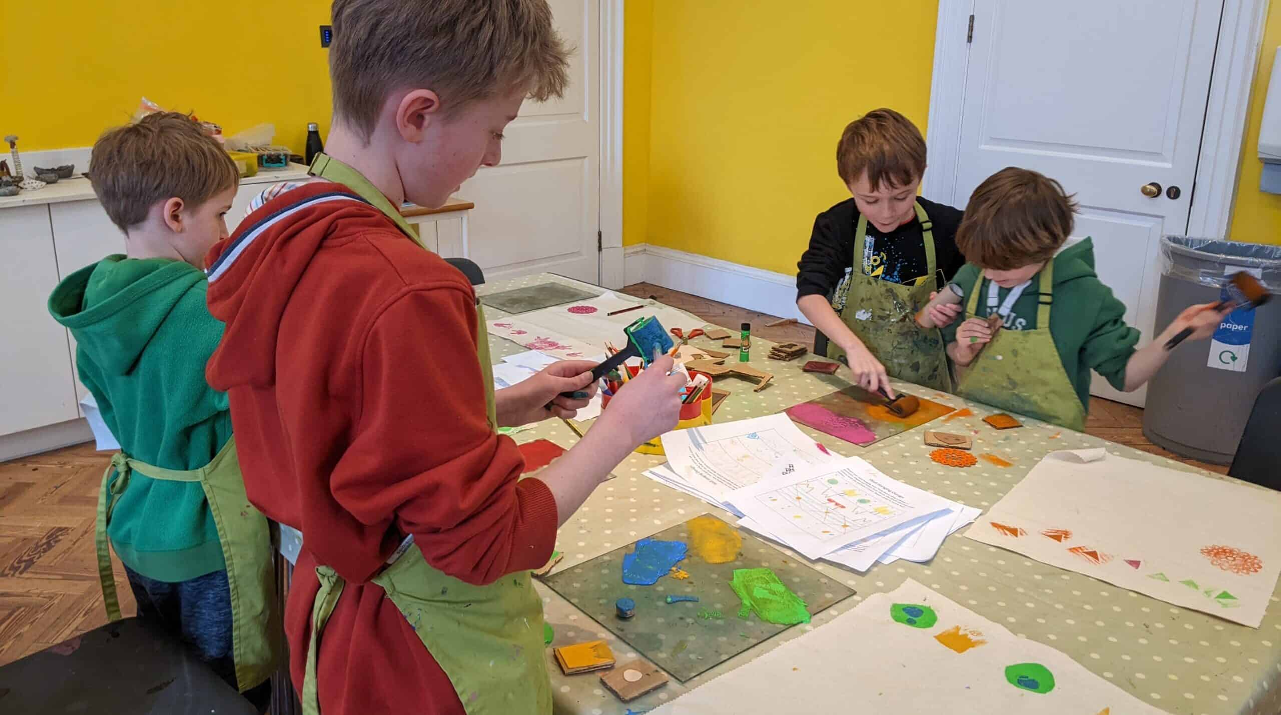 A group of 4 boys in aprons, engaging in a creative arts activity.