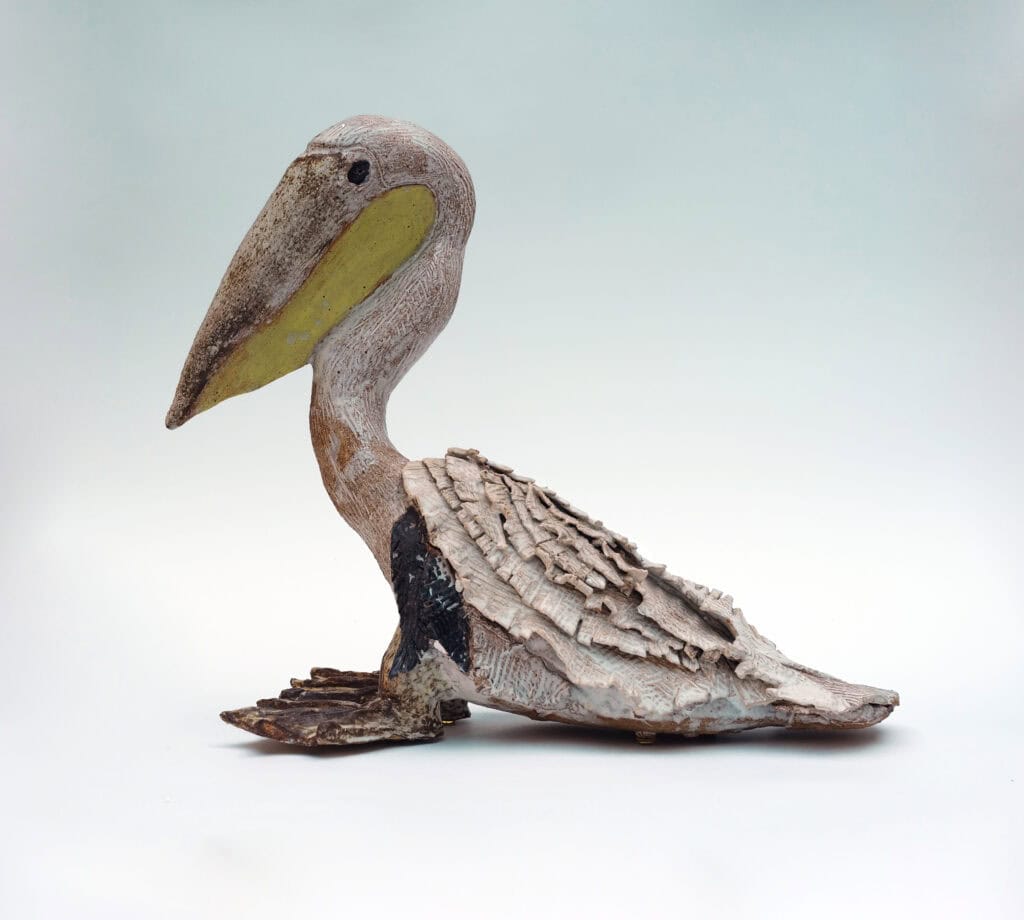 A sculpture of a grey pelican looking left, with a yellow beak
