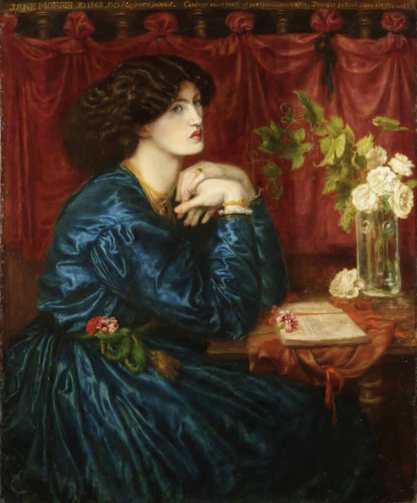 A lady with her hands folded sitting at a table with a book and flowers on it