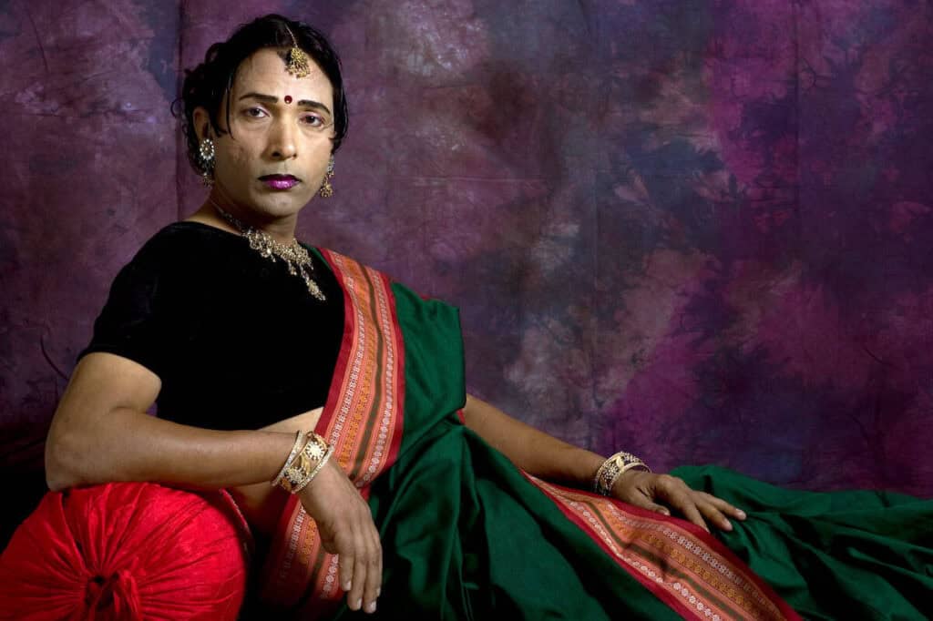 Sunil Gupta seated, wearing black and a red sari over it, looking at the camera