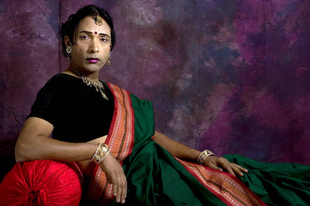 Sunil Gupta seated, wearing black and a red sari over it, looking at the camera