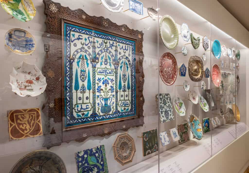Display case in the Peckham Corridor exhibition featuring ceramics and decorative tiles from the Holburne Museum collection.