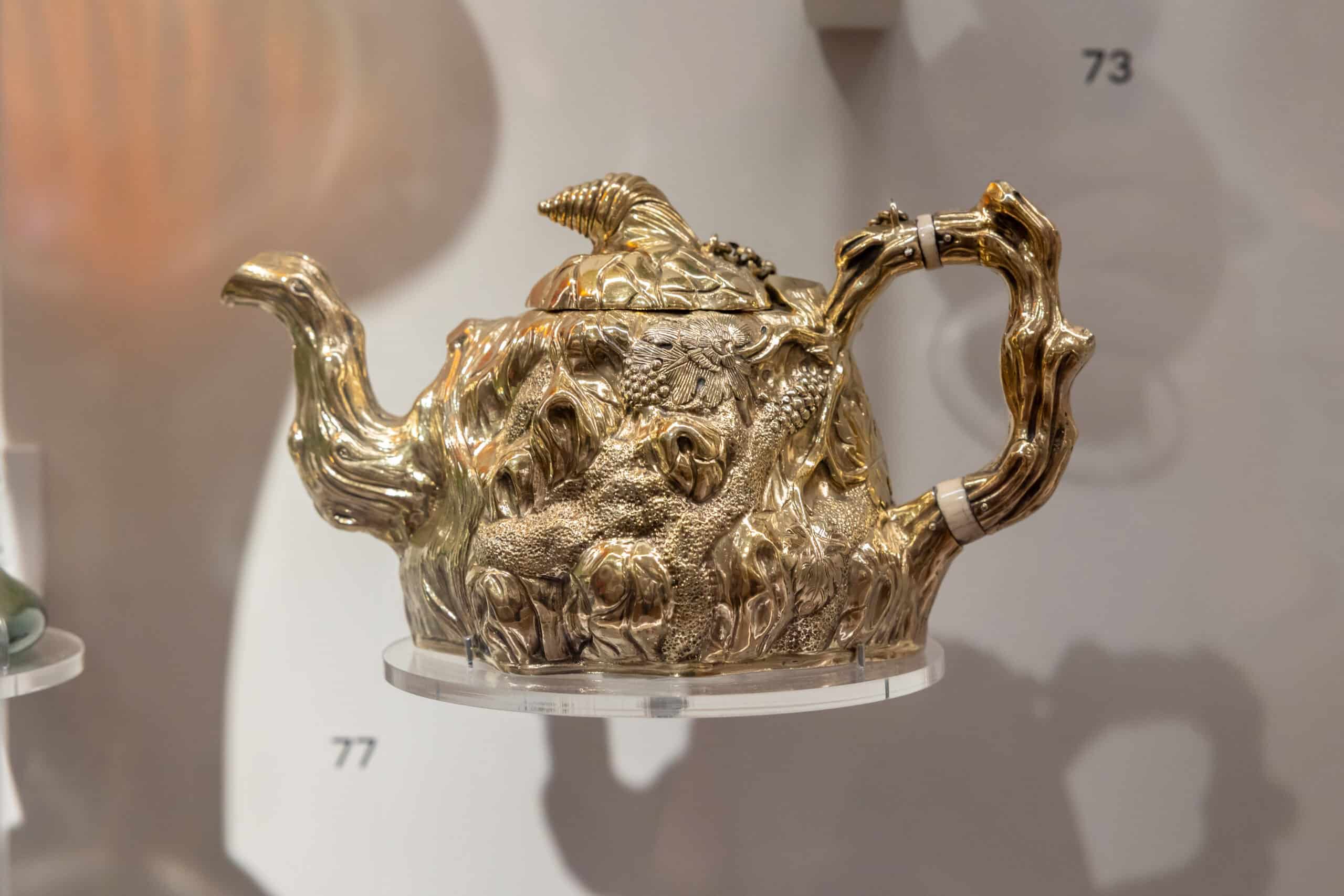 A silver gilt tea pot in the shape of a tree trunk, which is gold in colour. From the Peckham corridor display.