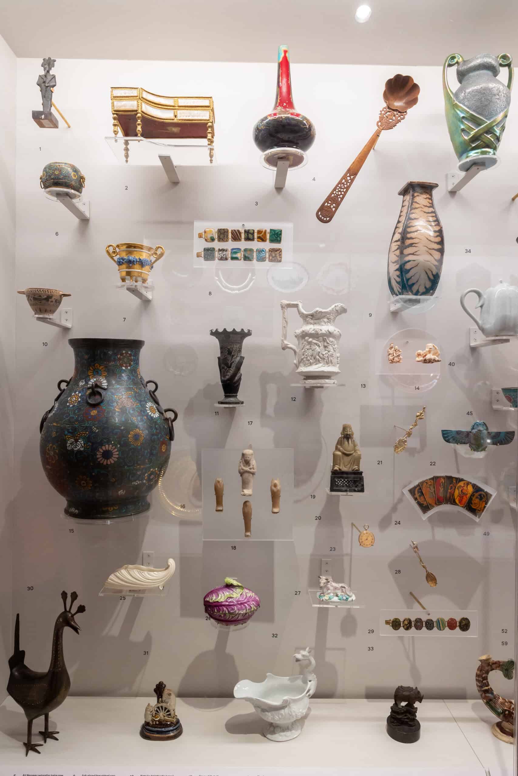 Display case in the Peckham Corridor exhibition showing a large blue vase and other ceramic objects, alongside a variety of decorative objects from the Holburne Museum collection.