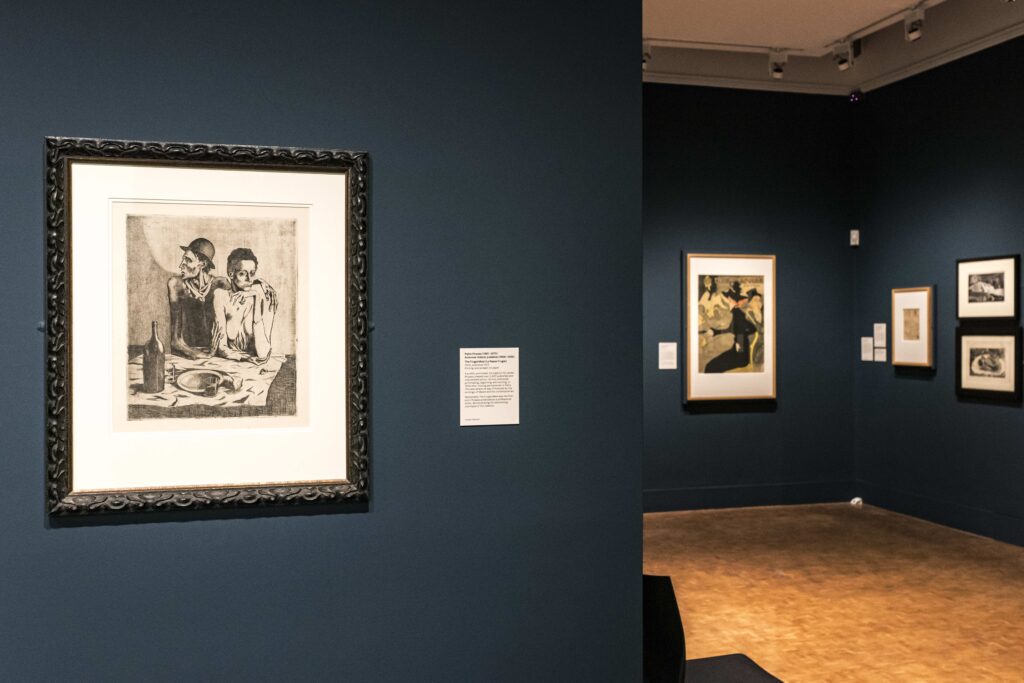 Photo showing a view of the gallery featuring dark blue walls and a number of monochrome prints