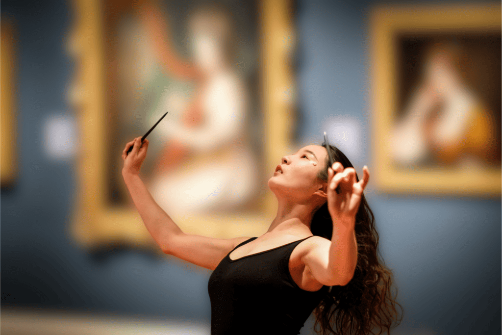 Photo showing a dancer with long dark hair, poised in front of large gold picture frames