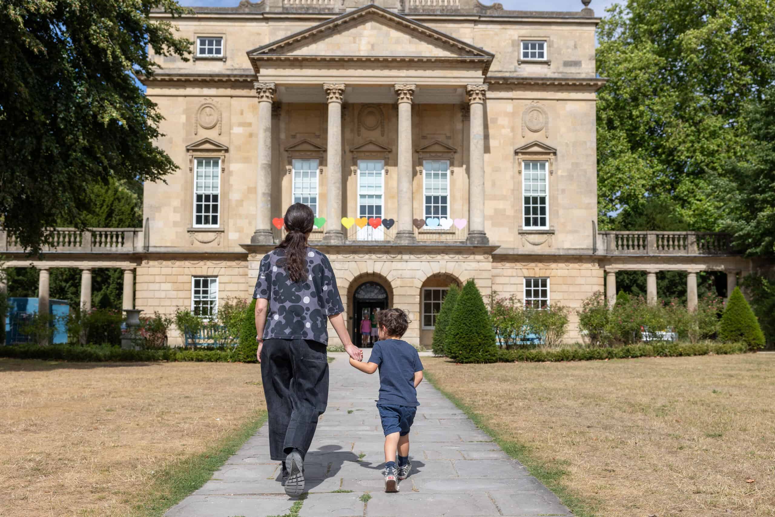 Photo showing a woman walking up the front path of the museum holding the hand of a small boy