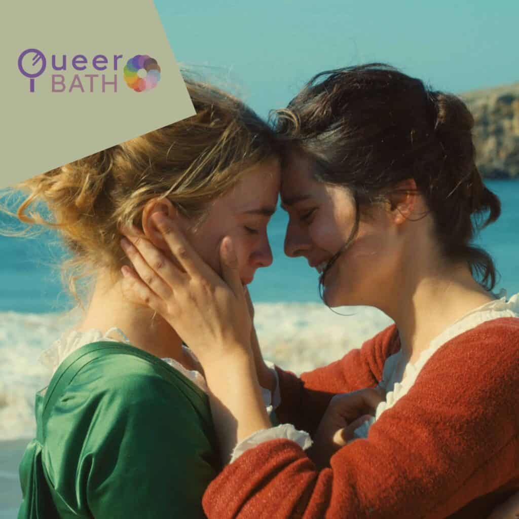 Two women facing each other on a beach, one holding the other's face, with the Queer Bath logo top left