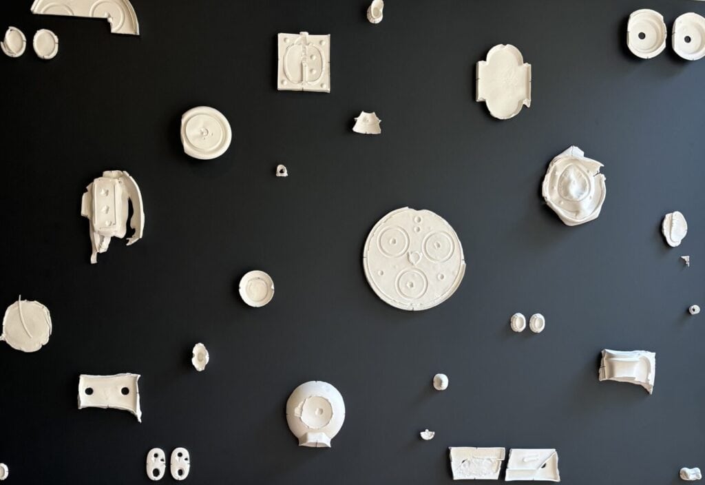 A museum display showing distorted white porcelain forms attached to a black background