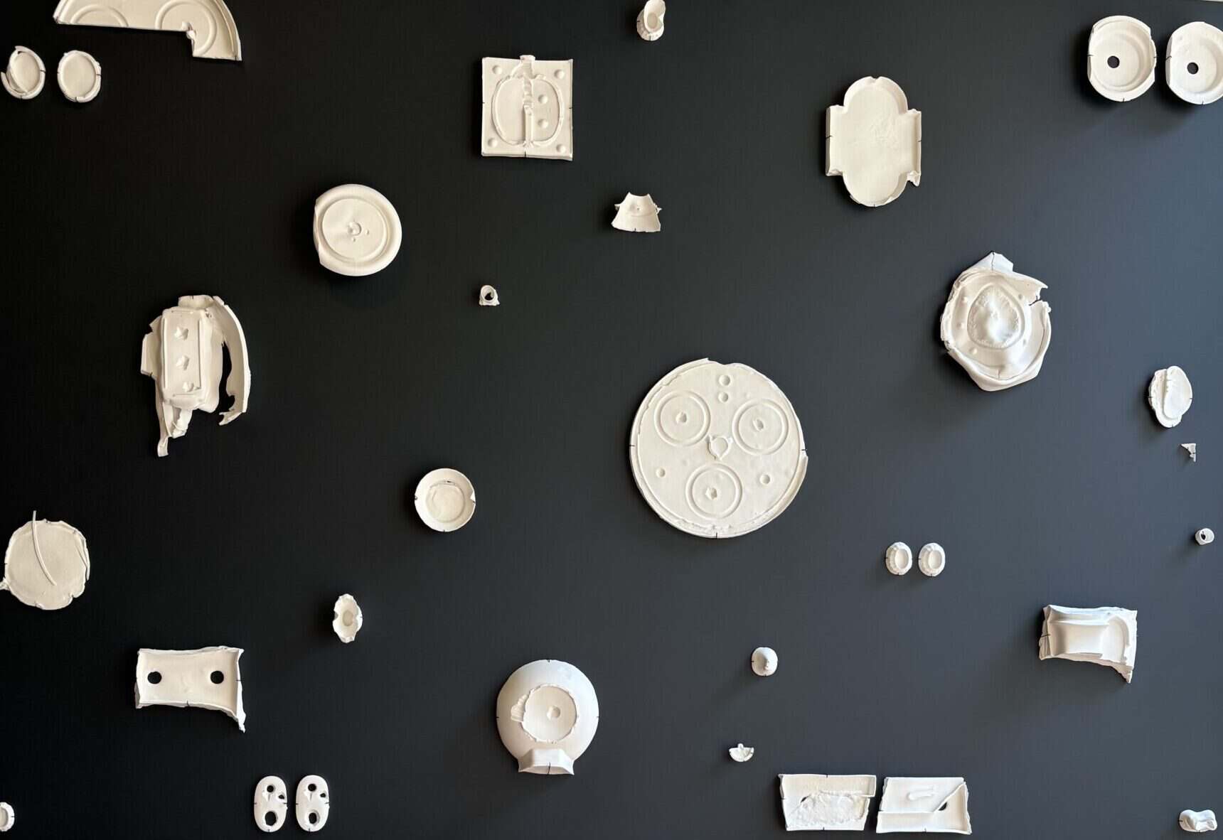 A museum display showing distorted white porcelain forms attached to a black background