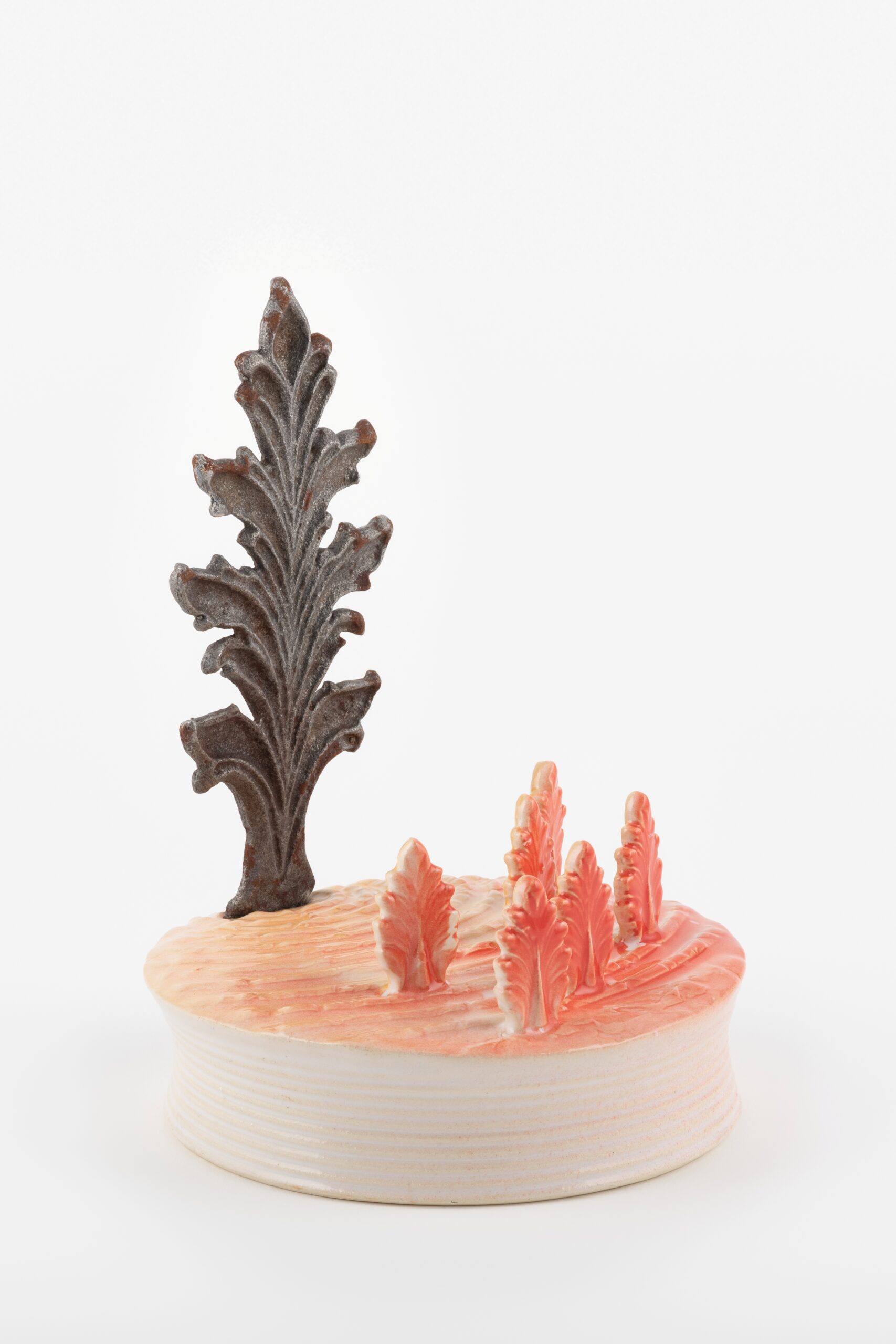 Photo showing a small round ceramic plinth with red and brown tree-like forms standing up