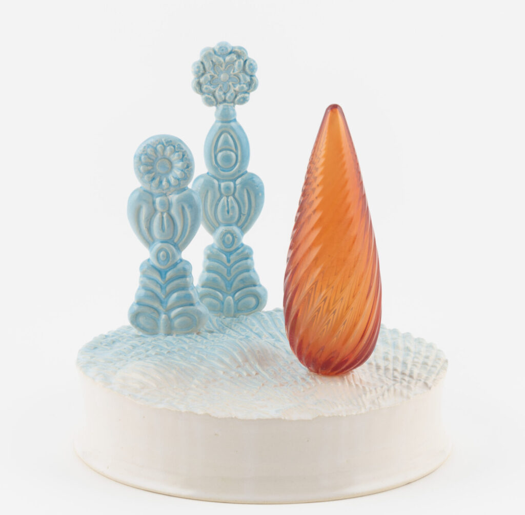 Photo showing a ceramic piece consisting of two blue coloured tree-like forms and an orange glass vessel