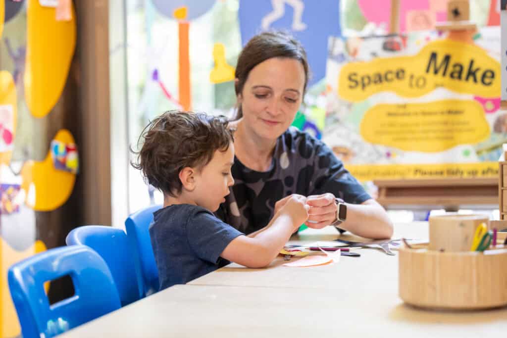 A mother and her young son are using scissors to cut out a paper shape
